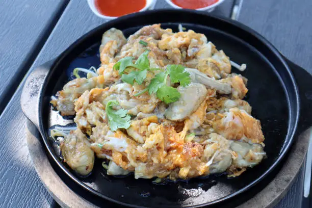 Photo of Thai style of Fried Oyster Omelette on black plate with spicy sauce.
