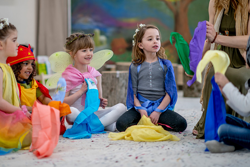 A small group of children play dress-up with each other in their Waldorf style classroom.  They are each dressed in various costumes and accessories as they use their imagination to play.