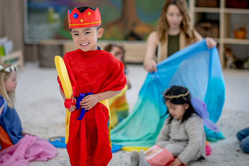 A small group of children play dress-up with each other in their Waldorf style classroom.  They are each dressed in various costumes and accessories as they use their imagination to play.