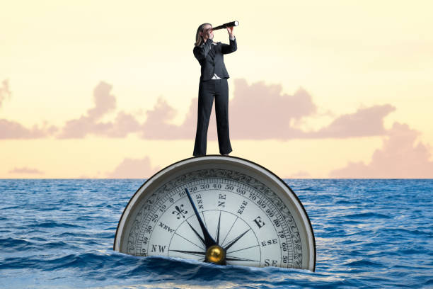 A woman standing on a large compass that is floating in the ocean looks through a spyglass into the distance.