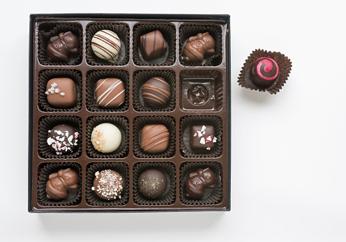 Open box of assorted, decorated gourmet chocolates, including, white, milk and dark chocolate isolated on white background.