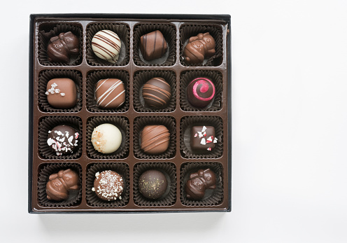Open box of assorted, decorated gourmet chocolates, including, white, milk and dark chocolate isolated on white background.