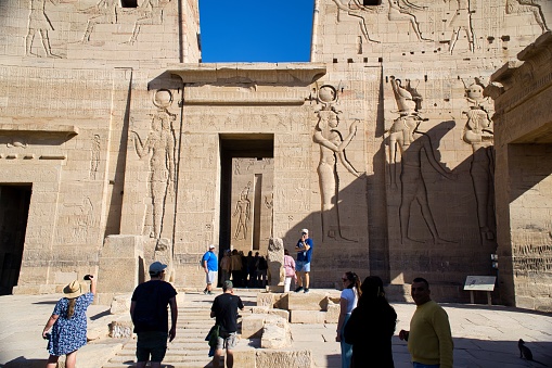 Female in vacation talking on a smart phone standing in front of the incredible Abu Simbel Temple rebuilt on the mountain in southern Egypt in Nubia next to Lake Nasser Egypt, Aswan, Abu Simbel