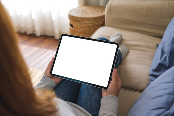 istock Mockup image of a woman holding digital tablet with blank desktop screen while lying on a sofa at home 1455147051