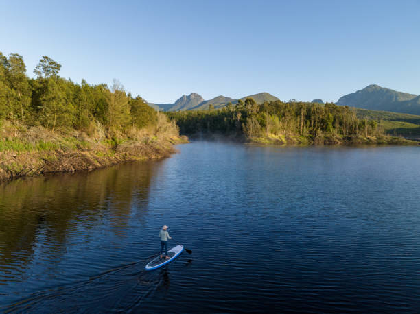 Paddleboarding on the Garden Route Dam near George Woman on a paddle board adventure on a pristine lake in the mountains near George, South Africa. Outdoor adventures along the Garden Route in the Western Cape george south africa stock pictures, royalty-free photos & images