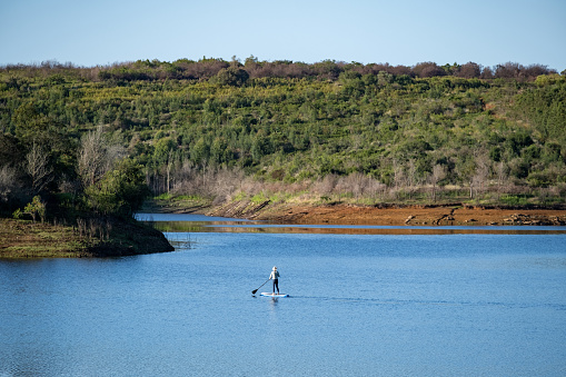 Woman on a paddle board adventure on a pristine lake in the mountains near George, South Africa. Outdoor adventures along the Garden Route in the Western Cape
