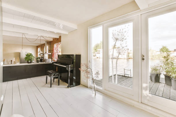 a living room with a piano and a large window a living room with white wood flooring and large windows looking out onto the water in the distance is a boat on the river sliding door stock pictures, royalty-free photos & images