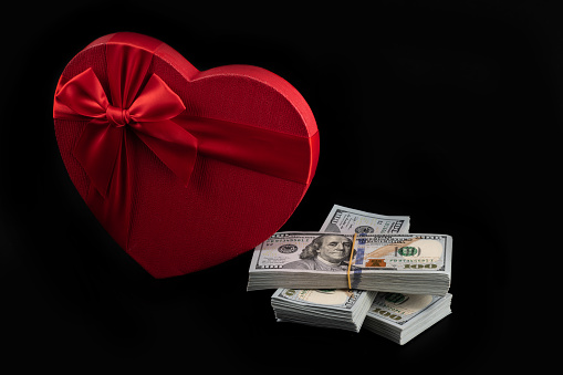 Gift box in the form of a symbol of a human heart and a bundle of banknotes in denominations of 100 US dollars