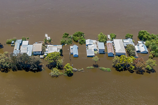 Aerial view row of treelined flooded houses and holiday shacks surrounded by murky brown floodwaters on River Murray, South Australia; Town planning issues with residences & vacation rentals built on floodplain. Murray Bridge, Jan 6, 2023