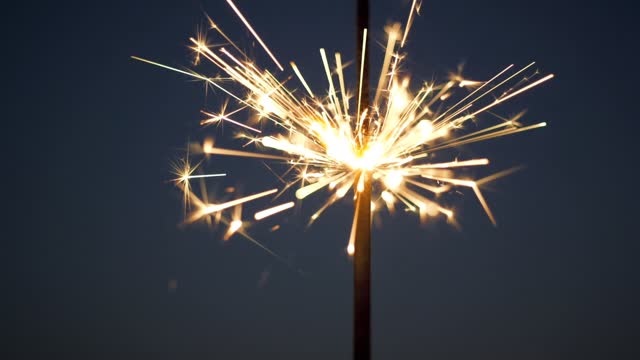 Firework sparkler burning over dark background. Slow motion shot of burning wand of Bengali fire against black Christmas background