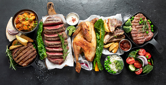 Various types of healthy cooked meat - beef, pork, chicken on a dark background with vegetables and salad. Top view.