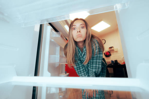 Confused Girl Looking into Her Empty Refrigerator Stressed woman having nothing to eat in her fridge fridge issues stock pictures, royalty-free photos & images