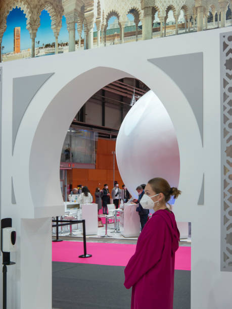 uma atendente feminina em vestido roxo em pé na tradicional porta marroquina do estande de marrocos na fitur 2022 - international tourism trade fair - fotografias e filmes do acervo