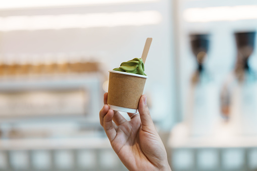 Woman hand holding green tea ice cream paper cup in cafe