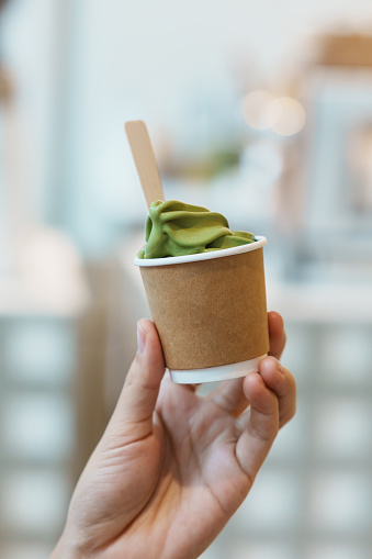 Woman hand holding green tea ice cream paper cup in cafe