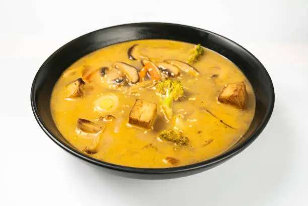 Photo of Tom yum. vegetarian soup in a black dish on a white background. a Thai dish