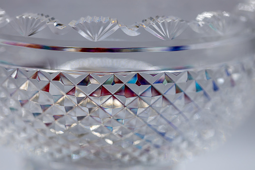 This image shows a defocused macro texture view of a shimmering antique lead crystal glass bowl with light reflecting diamond cuts and a scalloped edge.