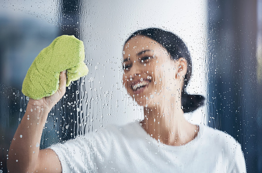 Cleaning, washing window and woman with cloth in hand to wipe water, detergent and cleaning products. Hygiene, housekeeping and happy girl doing housework, chores and  and wash or clean clear glass