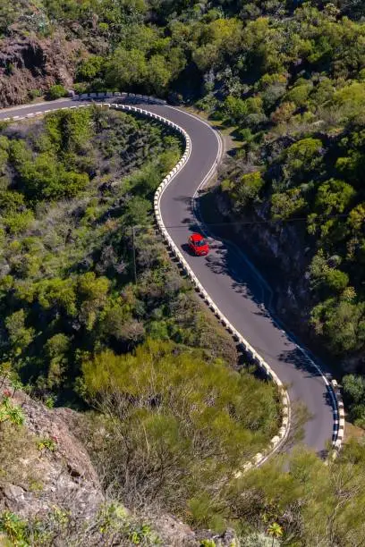 An aerial view of a red car on a winding road in the Masca canyon in the mountain municipality in the north of Tenerife, Canary Islands, Spain