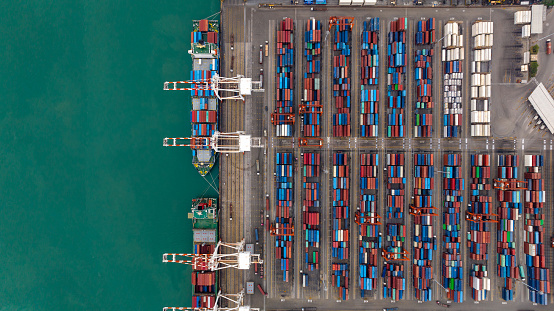 commercial port loading and unloading cargo from container ship import and export by crane for distributing goods by trailers transported to customers and dealers, aerial top view