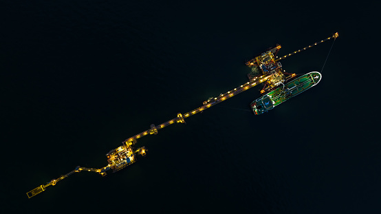 Aerial top view of oil tanker ship loading in port, Oil tanker ship under cargo operations on typical shore station with clearly visible mechanical loading arms and pipeline at night