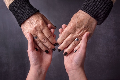 Young woman is holding a  senior woman's  hand on bed for help.