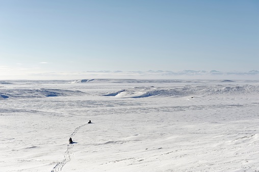 Two snowmobiles at a distance traveling overland near Yukon's Beaufort Sea coast and Porcupine Caribou herd birthing grounds Canada in winter