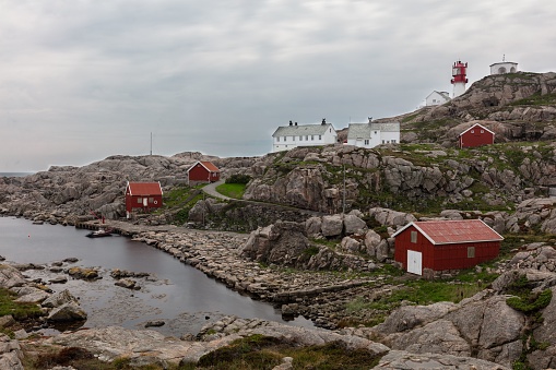 Landscape rocky coast of the sea, traditional wooden red Norwegian houses and the southern lighthouse Lindesnes fyr Norway in the evening