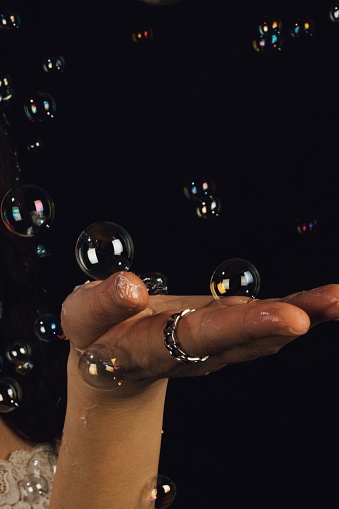 woman holding up flattened hand gesturing to floating, touchable bubbles on black background