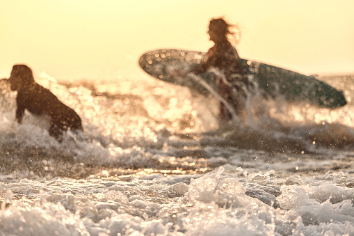 Close up of sea water with surfers in the background at sunset.