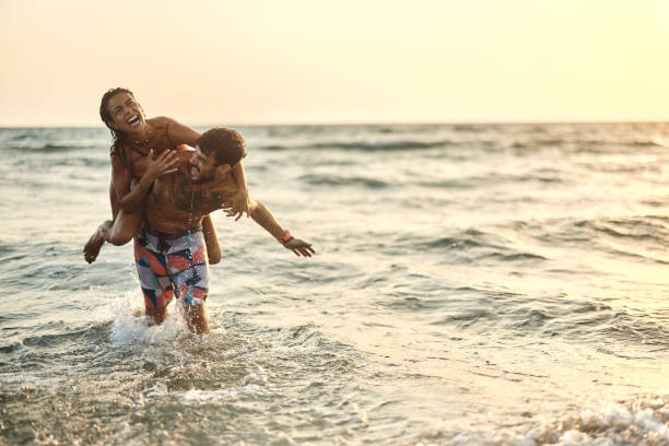 istock Cheerful couple having fun while piggybacking in sea at sunset. 1455203521