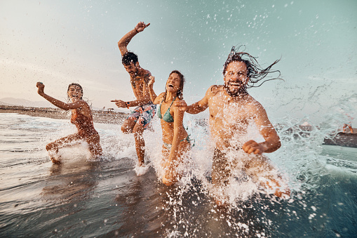 Cheerful friends having fun while running and splashing water during summer day at sea. Copy space.