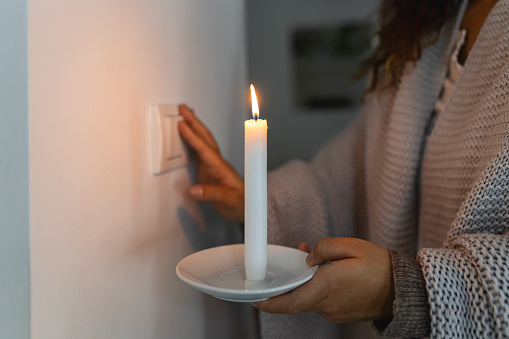 Energy crisis. Hand in complete darkness holding a candle trying to turn on light during a power outage. Blackout concept.