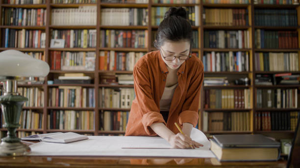 istock Young female engineer working on blueprint in university library, designing something 1455205290
