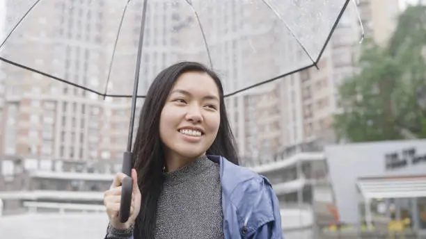 Beautiful asian woman without makeup walking under rain in the city, enjoying weather