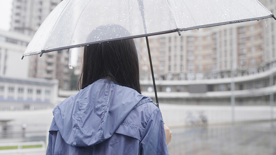 Woman standing in rain under transparent umbrella, bad weather in city, close up