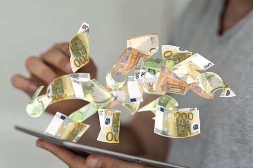 A hand with a tablet next 3D-visualized euro banknotes for business and financial concept .