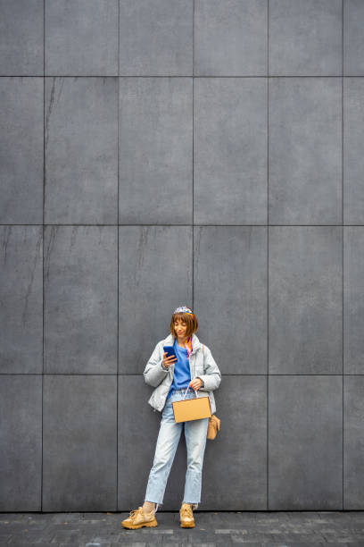 istock Woman with phone on gray wall background 1455206555