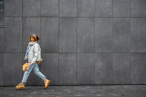Young stylish woman jumps while walking near the wall outdoors, wide view with copy space. Concept of city lifestyle and style