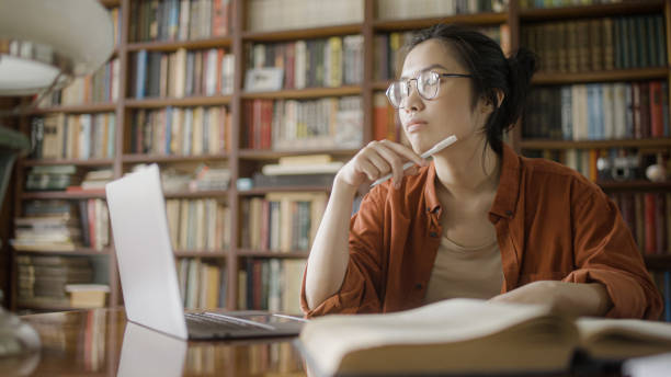 istock Asian student thinking over essay plot, working with books and laptop in the library 1455207437