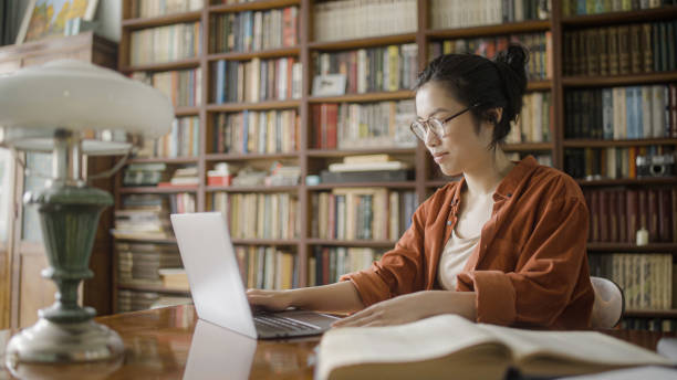 istock Young woman asian student sitting in library with laptop, studying or working 1455207546