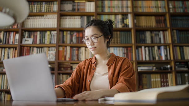 istock Concentrated female librarian working with books register on computer, keeping catalog 1455207624