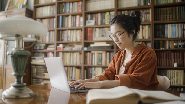 図書館でノートパソコンにタイピングし、ブログの記事を書くアジアの女性フリーランスライター - article ストックフォトと画像