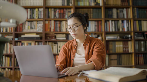 istock Asian woman student working on laptop, researching information at library archives 1455207792