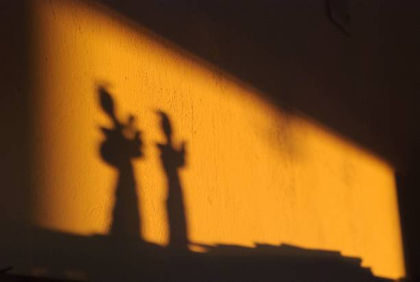 istock Silhouette of dolls on an orange wall under a light 1455207964