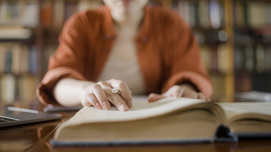 Woman doing research in a library, reading information in a large encyclopedia