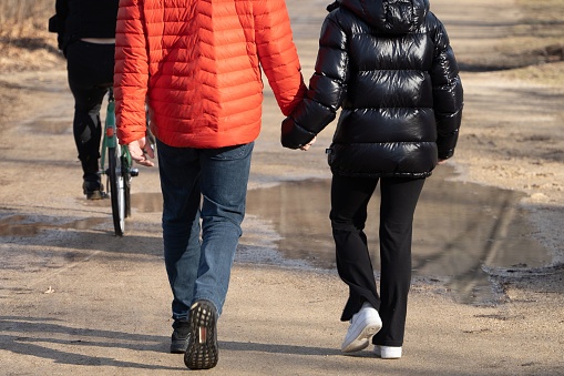 A closeup of a couple in down jackets walking along the street with puddles.