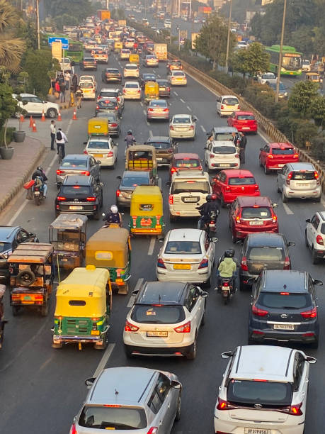 Stock photo showing view from overpass of traffic with motorcycles, cars and auto rickshaws seen gridlocked in a traffic jam running bumper to bumper on multilane highway. imagen de atasco de tráfico en autopista vista desde el paso elevado, motocicletas con pasajeros de pasajeros, autobuses, automóviles, rickshaws de automóviles estacionados en la autopista, carretera principal con barrera rayada, enfoque en primer plano