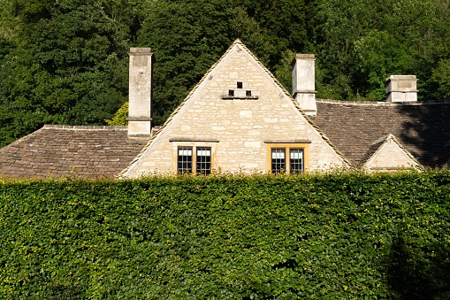 The view of the house roof behind the green hedge. Cotswolds,  England, UK.