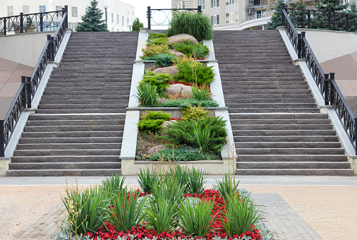 Modern landscaping of the park area with design paving slabs, stone stair steps, wrought iron railings and grassy terraces.